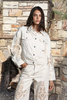 Woman wearing ALBA embroidered wide leg denim pants featuring structured cotton blend denim, high rise waist, classic four pocket design, intricate floral eyelet embroidery throughout the legs, relaxed wide leg silhouette, full length fit, button and zip fly closure, and belt loops along the waistline.