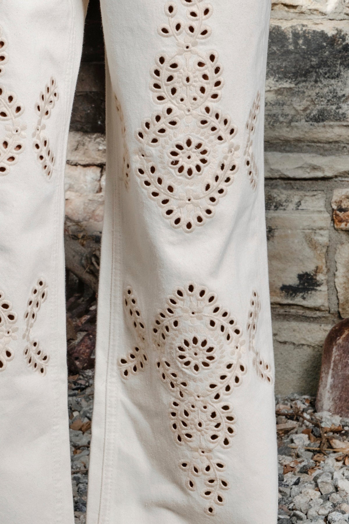 Woman wearing ALBA embroidered wide leg denim pants featuring structured cotton blend denim, high rise waist, classic four pocket design, intricate floral eyelet embroidery throughout the legs, relaxed wide leg silhouette, full length fit, button and zip fly closure, and belt loops along the waistline.