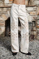 Woman wearing ALBA embroidered wide leg denim pants featuring structured cotton blend denim, high rise waist, classic four pocket design, intricate floral eyelet embroidery throughout the legs, relaxed wide leg silhouette, full length fit, button and zip fly closure, and belt loops along the waistline.