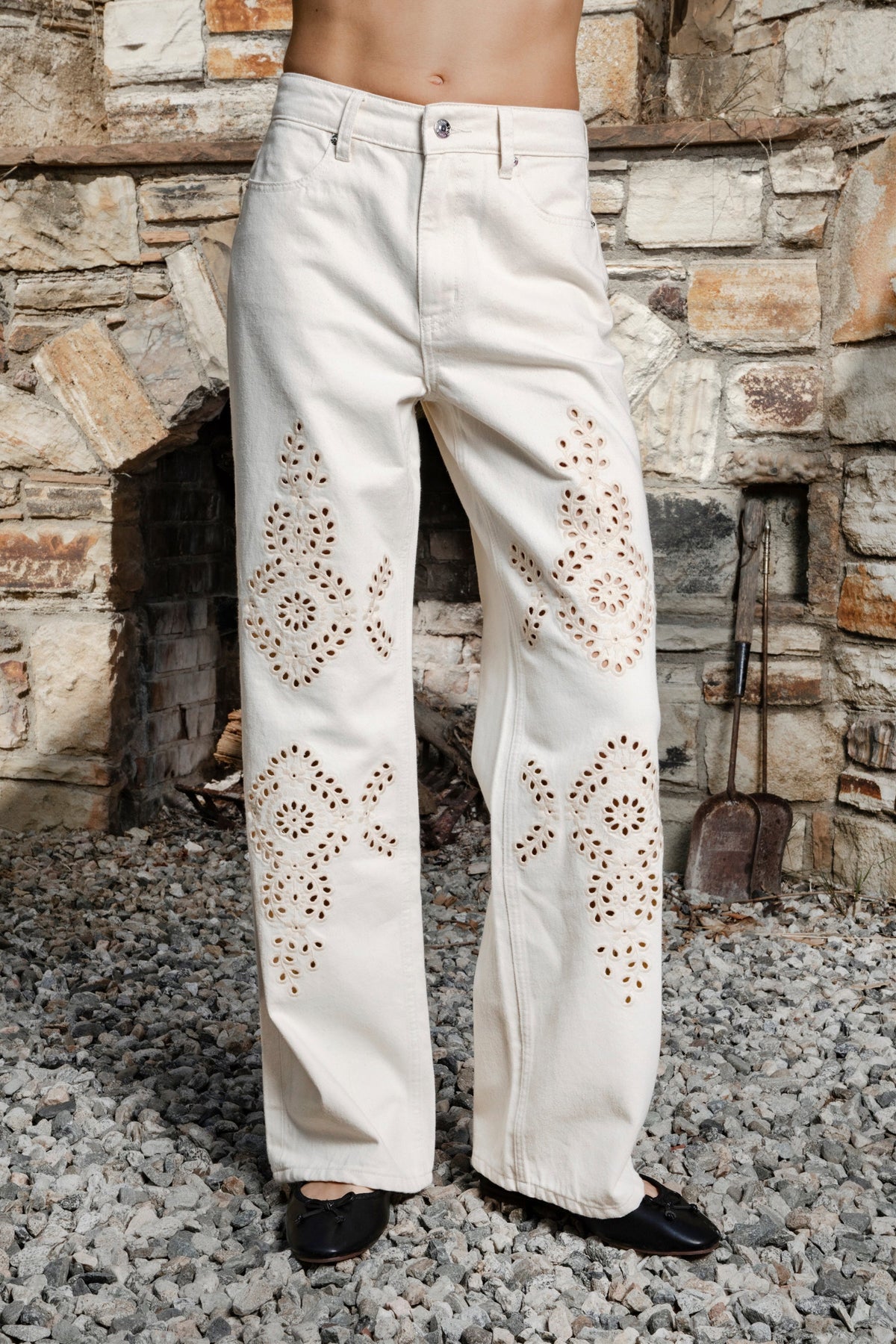 Woman wearing ALBA embroidered wide leg denim pants featuring structured cotton blend denim, high rise waist, classic four pocket design, intricate floral eyelet embroidery throughout the legs, relaxed wide leg silhouette, full length fit, button and zip fly closure, and belt loops along the waistline.