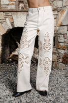 Woman wearing ALBA embroidered wide leg denim pants featuring structured cotton blend denim, high rise waist, classic four pocket design, intricate floral eyelet embroidery throughout the legs, relaxed wide leg silhouette, full length fit, button and zip fly closure, and belt loops along the waistline.