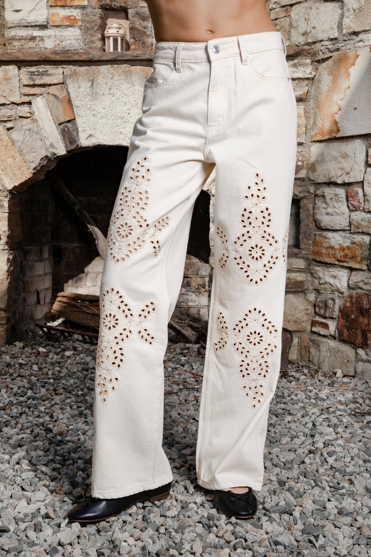 Woman wearing ALBA embroidered wide leg denim pants featuring structured cotton blend denim, high rise waist, classic four pocket design, intricate floral eyelet embroidery throughout the legs, relaxed wide leg silhouette, full length fit, button and zip fly closure, and belt loops along the waistline.