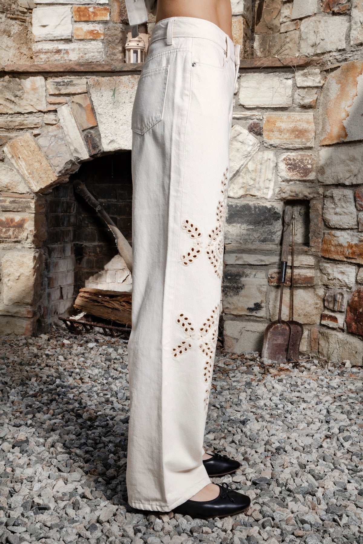 Woman wearing ALBA embroidered wide leg denim pants featuring structured cotton blend denim, high rise waist, classic four pocket design, intricate floral eyelet embroidery throughout the legs, relaxed wide leg silhouette, full length fit, button and zip fly closure, and belt loops along the waistline.