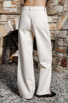 Woman wearing ALBA embroidered wide leg denim pants featuring structured cotton blend denim, high rise waist, classic four pocket design, intricate floral eyelet embroidery throughout the legs, relaxed wide leg silhouette, full length fit, button and zip fly closure, and belt loops along the waistline.