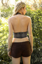 Woman wearing TIC TOC TG31902 CALEXA distressed washed denim halter top in a washed black denim finish, featuring a deep halter neckline, distressed frayed trim, front faux eyelet belt detail, contrast white stitching, cropped fitted silhouette, and low back zipper closure for an edgy western festival look.