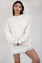 Woman wearing a white sweater and skirt against a plain background