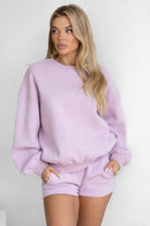 Woman wearing a lavender sweatshirt and shorts set against a white background