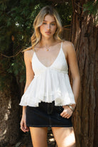 Woman wearing TIC TOC TH31010 CYRUS crinkle gauze cami top featuring a plunging V-neckline, adjustable shoulder straps, tiered babydoll silhouette, asymmetrical raw-cut hem, and soft lightweight cotton gauze texture for a western-inspired summer look.