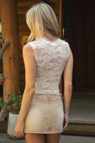 Women wearing TIC TOC IRIS Stretch Lace Tank Top in cream featuring a high mock neckline, open keyhole chest cutout, and sheer floral lace design paired with brown mini skirt outdoors. 