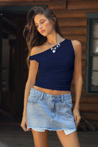 Woman wearing a navy blue top and denim skirt standing in front of a wooden building.