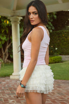 Woman wearing a light pink top and white ruffled bloomers outdoors.