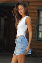 Woman wearing a white top and denim shorts standing in front of a wooden cabin.