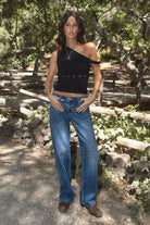 Women wearing TIC TOC SHANTAL One Shoulder Top in black with twisted strap, ruched seams, and studded torso detail paired with a denim blue jeans  and boots. 