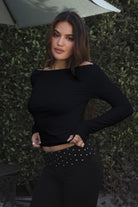 Model wearing TIC TOC TH31573BA RAYAE asymmetric off-the-shoulder jersey top with wide neckline and draped long sleeves paired with polka dot black capri pants in an outdoor setting. 
