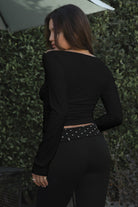 Model wearing TIC TOC TH31573BA RAYAE asymmetric off-the-shoulder jersey top with wide neckline and draped long sleeves paired with polka dot black capri pants in an outdoor setting. 