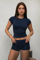 Woman wearing TIC TOC TH31680BA-NYLEE-SS NYLEE soft span jersey short sleeve top featuring a classic crew neckline with cap sleeves, cropped slim silhouette, smooth second-skin fit, and clean minimal seaming, styled with matching NYLEE bottoms in a coordinated lounge/athleisure set.
