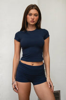 Woman wearing TIC TOC TH31680BA-NYLEE-SS NYLEE soft span jersey short sleeve top featuring a classic crew neckline with cap sleeves, cropped slim silhouette, smooth second-skin fit, and clean minimal seaming, styled with matching NYLEE bottoms in a coordinated lounge/athleisure set.