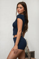 Woman wearing TIC TOC TH31680BA-NYLEE-SS NYLEE soft span jersey short sleeve top featuring a classic crew neckline with cap sleeves, cropped slim silhouette, smooth second-skin fit, and clean minimal seaming, styled with matching NYLEE bottoms in a coordinated lounge/athleisure set.