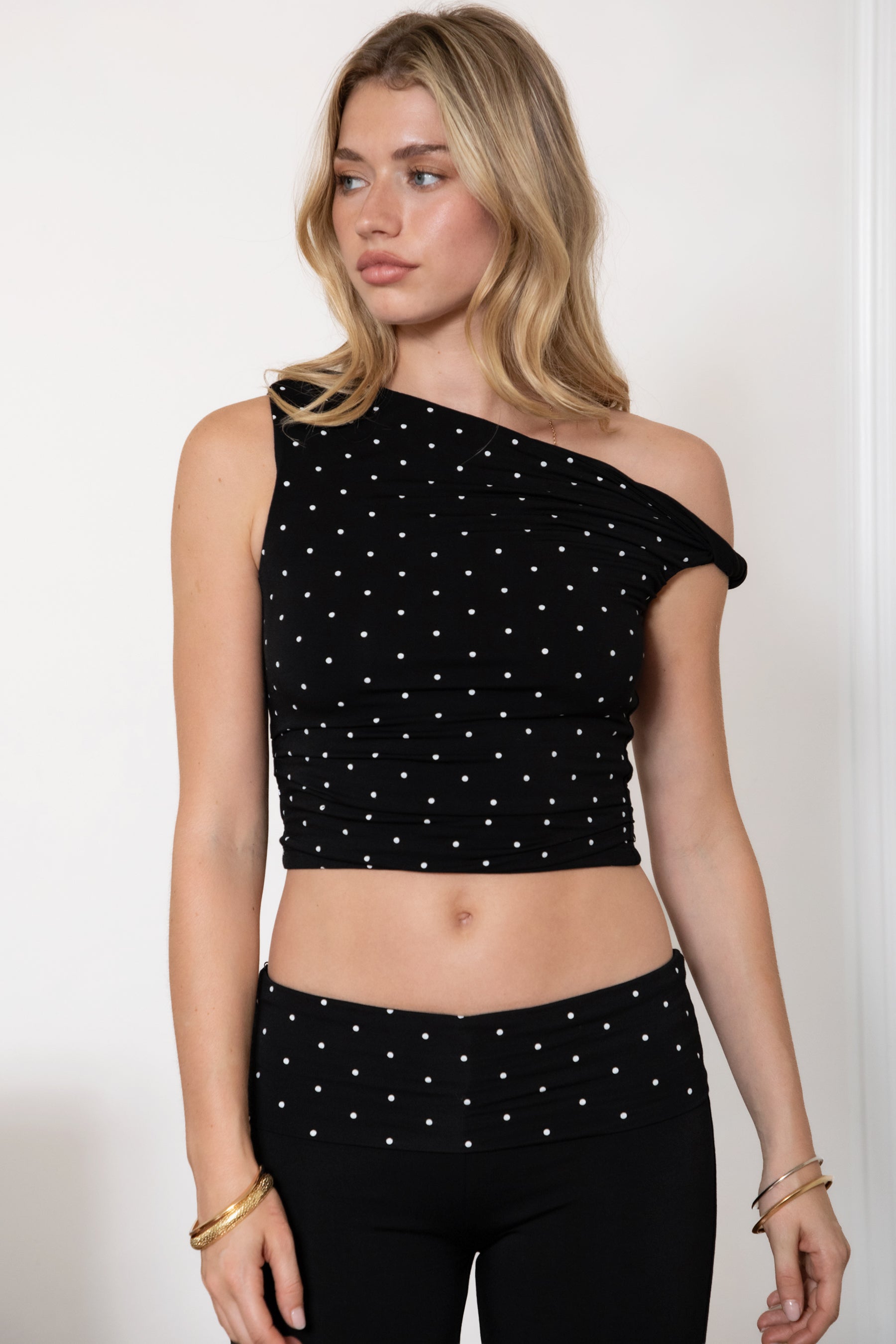 Woman wearing TIC TOC TH31776-JAIME-TP JAIME lightweight one shoulder polka dot top featuring a soft micro polka dot stretch fabric, asymmetrical off-the-shoulder neckline, twist strap detail, side ruching, and a slim hip-length silhouette for a chic day-to-night look.