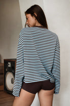 Woman wearing TIC TOC TH31849 MARLOWE striped long sleeve top with a classic crew neckline, relaxed semi-oversized fit, easy drop shoulders, and soft horizontal stripes paired with dark denim jeans in a casual outdoor street setting.