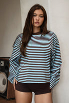 Woman wearing TIC TOC TH31849 MARLOWE striped long sleeve top with a classic crew neckline, relaxed semi-oversized fit, easy drop shoulders, and soft horizontal stripes paired with dark denim jeans in a casual outdoor street setting.
