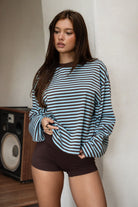 Woman wearing TIC TOC TH31849 MARLOWE striped long sleeve top with a classic crew neckline, relaxed semi-oversized fit, easy drop shoulders, and soft horizontal stripes paired with dark denim jeans in a casual outdoor street setting.