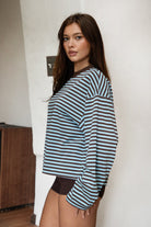 Woman wearing TIC TOC TH31849 MARLOWE striped long sleeve top with a classic crew neckline, relaxed semi-oversized fit, easy drop shoulders, and soft horizontal stripes paired with dark denim jeans in a casual outdoor street setting.