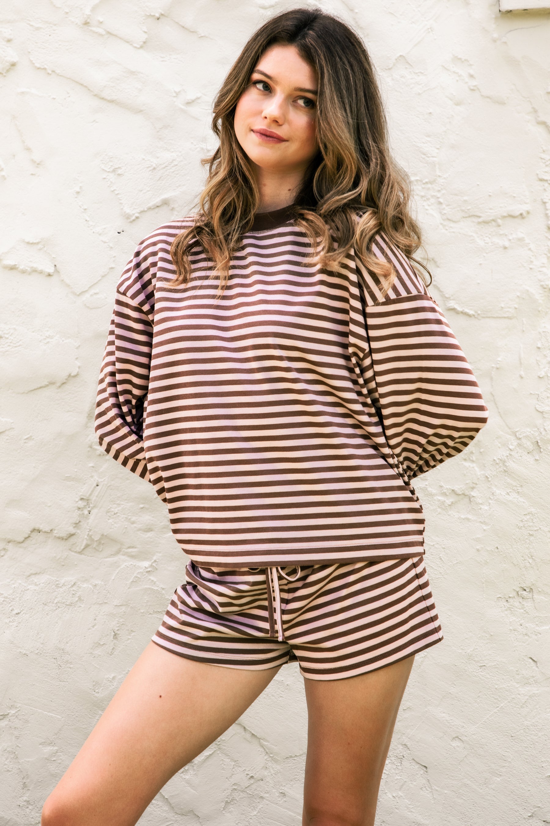 Woman wearing TIC TOC TH31849 MARLOWE striped long sleeve top with a classic crew neckline, relaxed semi-oversized fit, easy drop shoulders, and soft horizontal stripes paired with dark denim jeans in a casual outdoor street setting.