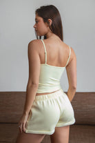 Woman wearing TIC TOC TH31906BA-NYLEE-CAM NYLEE Soft Span Jersey Cami Top in a dark neutral tone, featuring a delicate V-neckline with slim cami straps, clean minimal seaming, cropped second-skin silhouette, and smooth stretch fit, styled with coordinating NYLEE bottoms for a matching lounge/athleisure set.