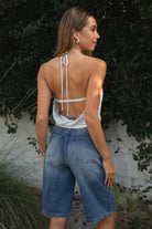Woman wearing TIC TOC TH31911-TERAYA TERAYA open back halter neck top featuring an adjustable halter neckline, eyelet front button detail, deep asymmetrical front cutout, soft stretch jersey fabric, slim feminine fit, and open cowl back silhouette, styled with low-rise bottoms for a Y2K-inspired night-out and festival look