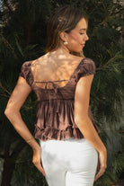 Woman wearing TIC TOC TH31912-AVELINE AVELINE V-neck boho lace trim babydoll top featuring a deep V-neckline with lace trim, mini puff sleeves with soft elastic cuffs, front button detail at the bodice, tiered babydoll silhouette with ruffle hem, and a smocked fitted back with adjustable bow tie in lightweight cotton voile, styled with denim for a soft boho western romantic everyday look