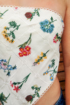 Woman wearing FLORELLE floral embroidered bandana crop tank top featuring delicate floral embroidery on textured linen blend fabric, classic cropped bandana silhouette, adjustable self tie back, and scalloped picot trim for summer resort and festival styling.
