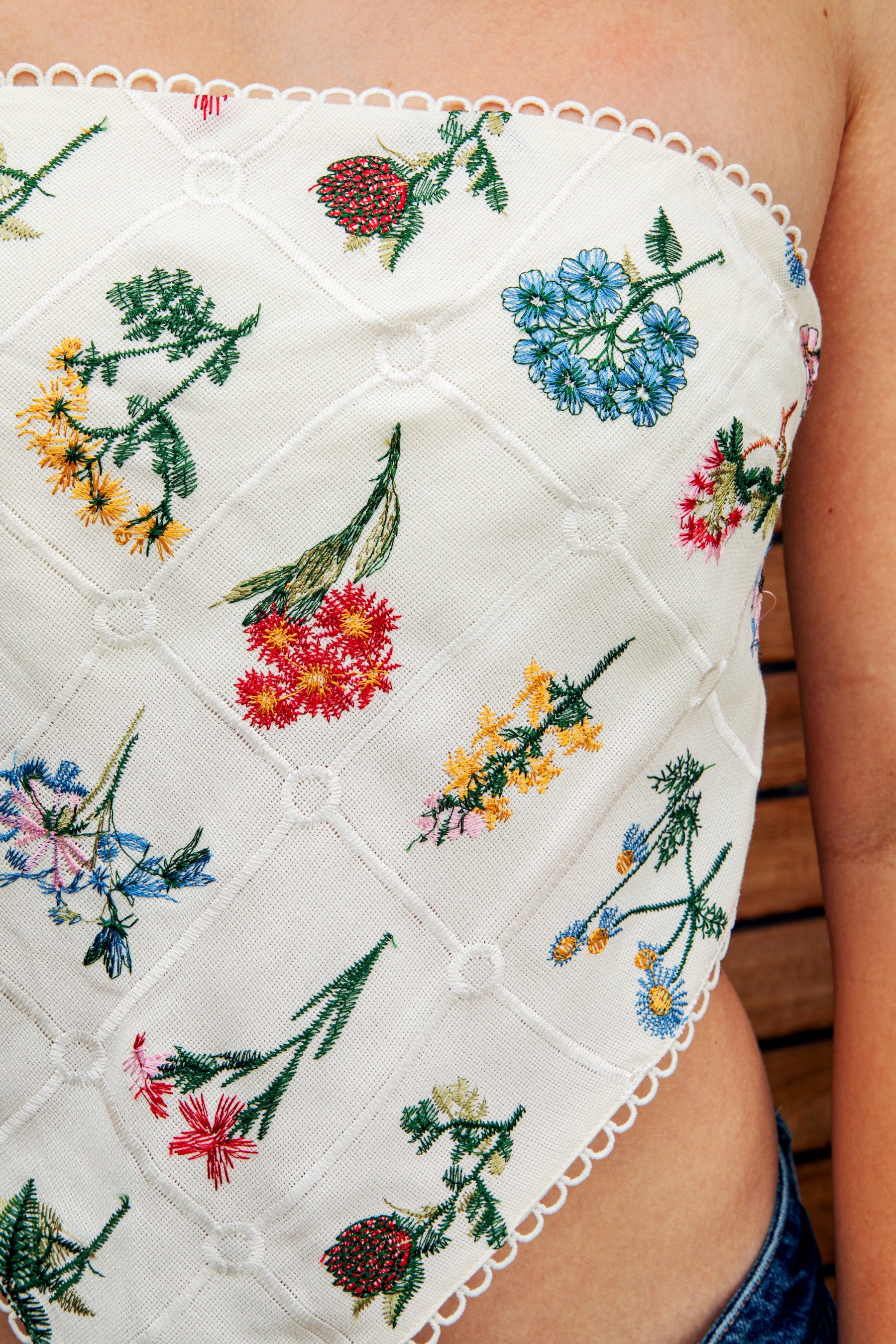Woman wearing FLORELLE floral embroidered bandana crop tank top featuring delicate floral embroidery on textured linen blend fabric, classic cropped bandana silhouette, adjustable self tie back, and scalloped picot trim for summer resort and festival styling.