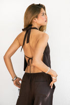 Woman wearing SOLSTICE viscose linen split front halter top featuring a deep split front detail with under bust strap accent, open back with adjustable self tie closure, halter neckline, and lightweight viscose linen fabric with relaxed draped fit for resort styling.