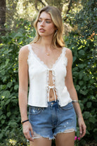 Woman wearing BLOOM scalloped lace split front cami top featuring a V-neckline with delicate lace trim, front split detail with adjustable bow tie closure, slim adjustable shoulder straps, back adjustable strap, and a lightweight viscose linen blend fully lined with smooth rayon challis.