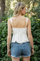 Woman wearing BLOOM scalloped lace split front cami top featuring a V-neckline with delicate lace trim, front split detail with adjustable bow tie closure, slim adjustable shoulder straps, back adjustable strap, and a lightweight viscose linen blend fully lined with smooth rayon challis.