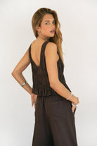 Woman wearing SOLSTICE ruched tie front round neck cami top featuring soft ruched texture throughout the body, three self-tie front closures, deep round neckline, wide shoulder straps, and a lightweight viscose linen blend with ruffled hem detail for relaxed resort styling.
