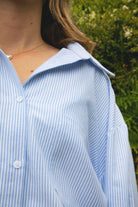 Woman wearing BLAIRE stripe oversized button down shirt featuring classic stripe oxford fabric, relaxed oversized silhouette, collared neckline, full front button closure, dropped shoulders, long sleeves with button cuffs, and functional chest pocket for effortless layering.
