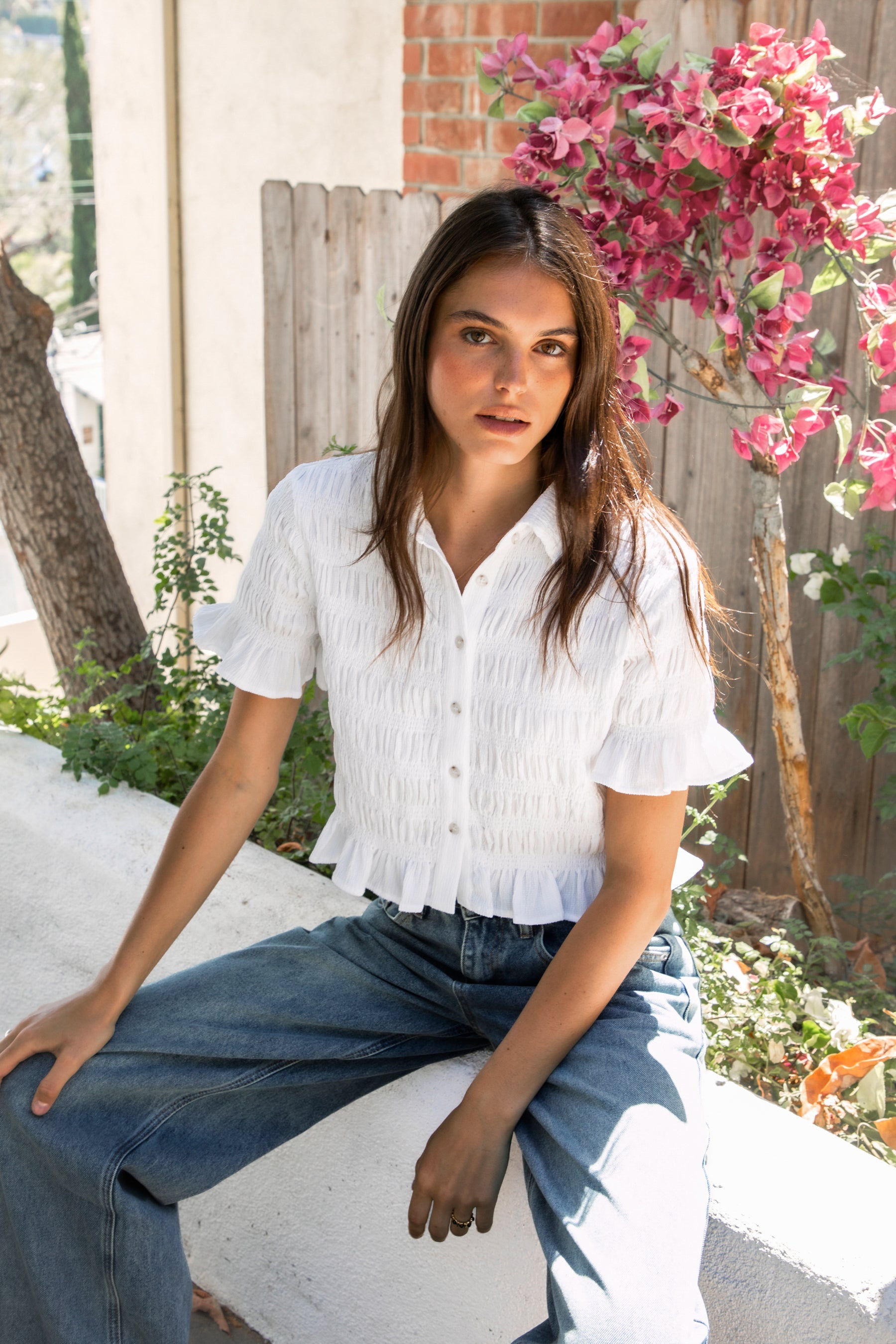 Woman wearing LISETTE smocked button front collared crop top featuring allover smocked textured fabric, soft stretch fit, classic collared neckline, functional button front closure, short puff sleeves with flounce ruffle cuffs, and a cropped silhouette with delicate ruffle hem.