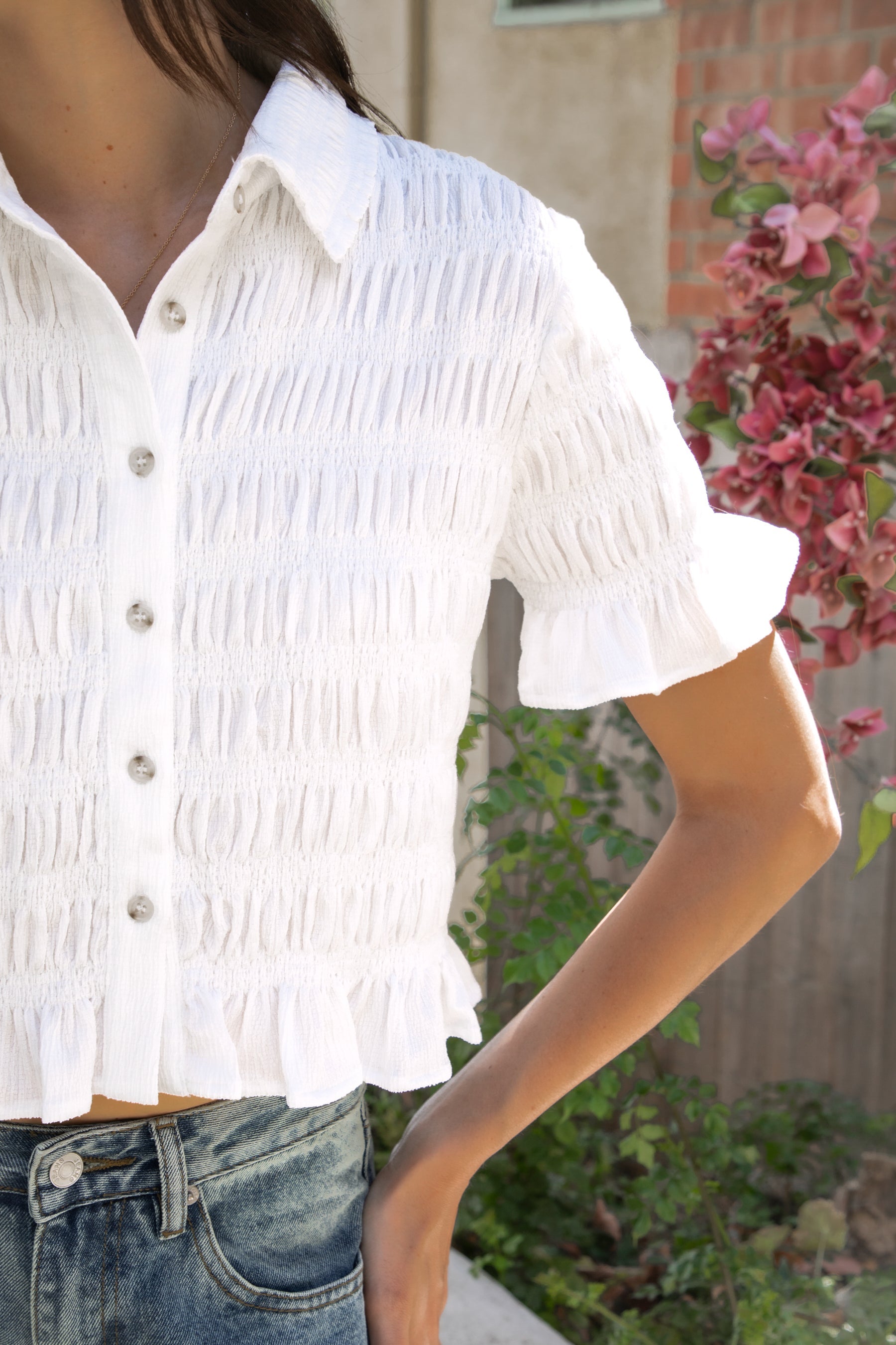 Woman wearing LISETTE smocked button front collared crop top featuring allover smocked textured fabric, soft stretch fit, classic collared neckline, functional button front closure, short puff sleeves with flounce ruffle cuffs, and a cropped silhouette with delicate ruffle hem.