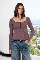 Woman wearing ELODY striped babydoll square neck henley peplum top featuring soft striped knit fabric, wide scoop neckline with contrast trim, henley inspired front placket with metal snap details, fitted bodice, empire waist seam, flared peplum hem, and long fitted sleeves.