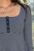 Woman wearing ELODY striped babydoll square neck henley peplum top featuring soft striped knit fabric, wide scoop neckline with contrast trim, henley inspired front placket with metal snap details, fitted bodice, empire waist seam, flared peplum hem, and long fitted sleeves.