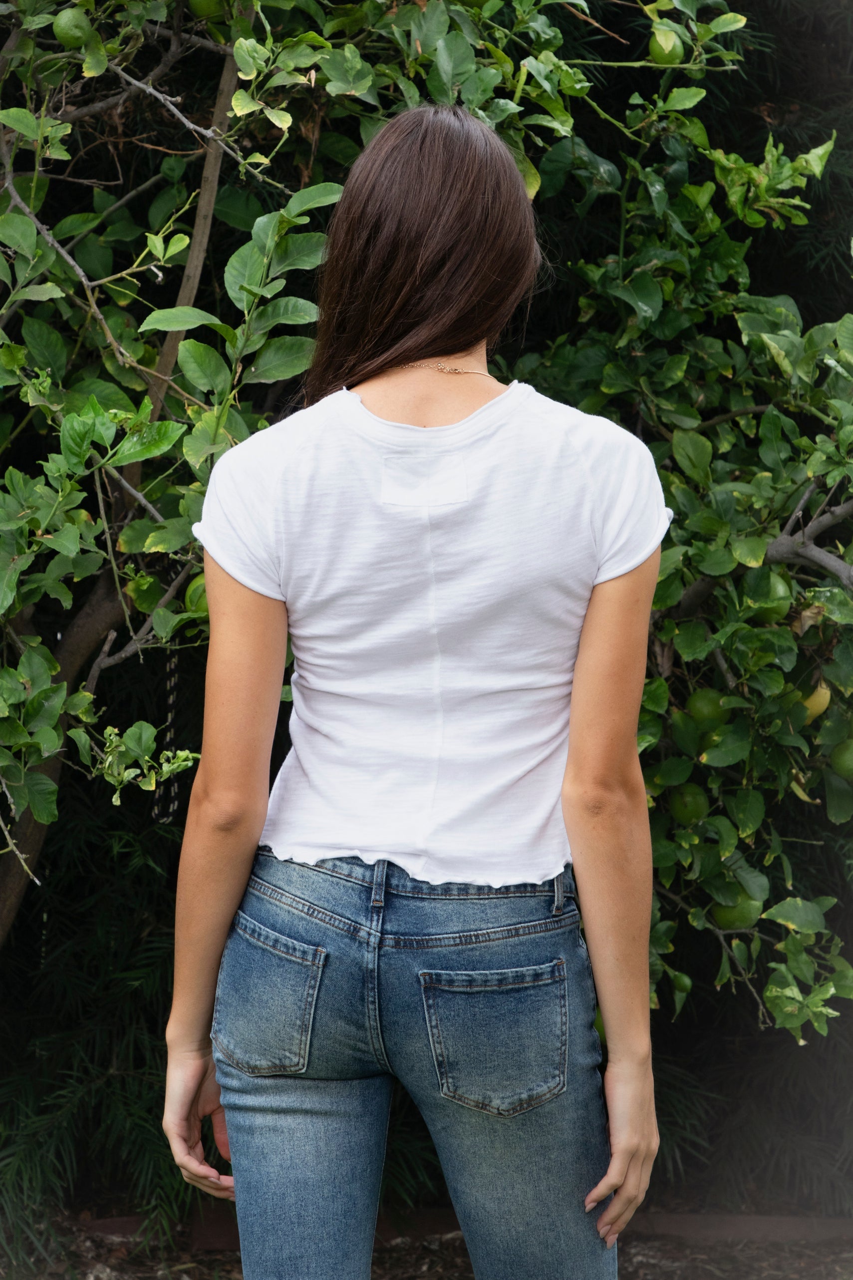 Woman wearing LENI cotton slub lettuce hem baby tee featuring soft lightweight cotton slub fabric, classic crew neckline, short cap sleeves, fitted baby tee silhouette, slightly cropped length, and delicate lettuce edge hem for effortless casual styling with denim.