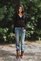 Woman wearing EMMELINE ruched lace long sleeve top featuring sheer floral stretch lace, fitted feminine silhouette, deep V neckline with scalloped lace trim, ruched detailing through the front and sides, soft mesh bust lining, sheer fitted long sleeves, flared lace trimmed cuffs, and scalloped hem finish.