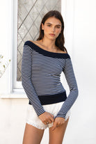 Woman wearing ALIZEE contrast striped off shoulder long sleeve top featuring classic striped jersey fabric, wide solid rib neckline, fitted feminine silhouette, long fitted sleeves, contrast solid rib hem band, hip length fit, and soft stretch construction for casual everyday and transitional styling.