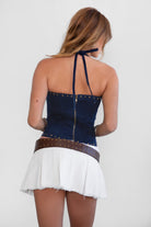 Woman wearing TIC TOC TA31346 RAELY stretch denim embroidered western corset top with halter tie and lace-up front detail with a white mini skirt and belt.