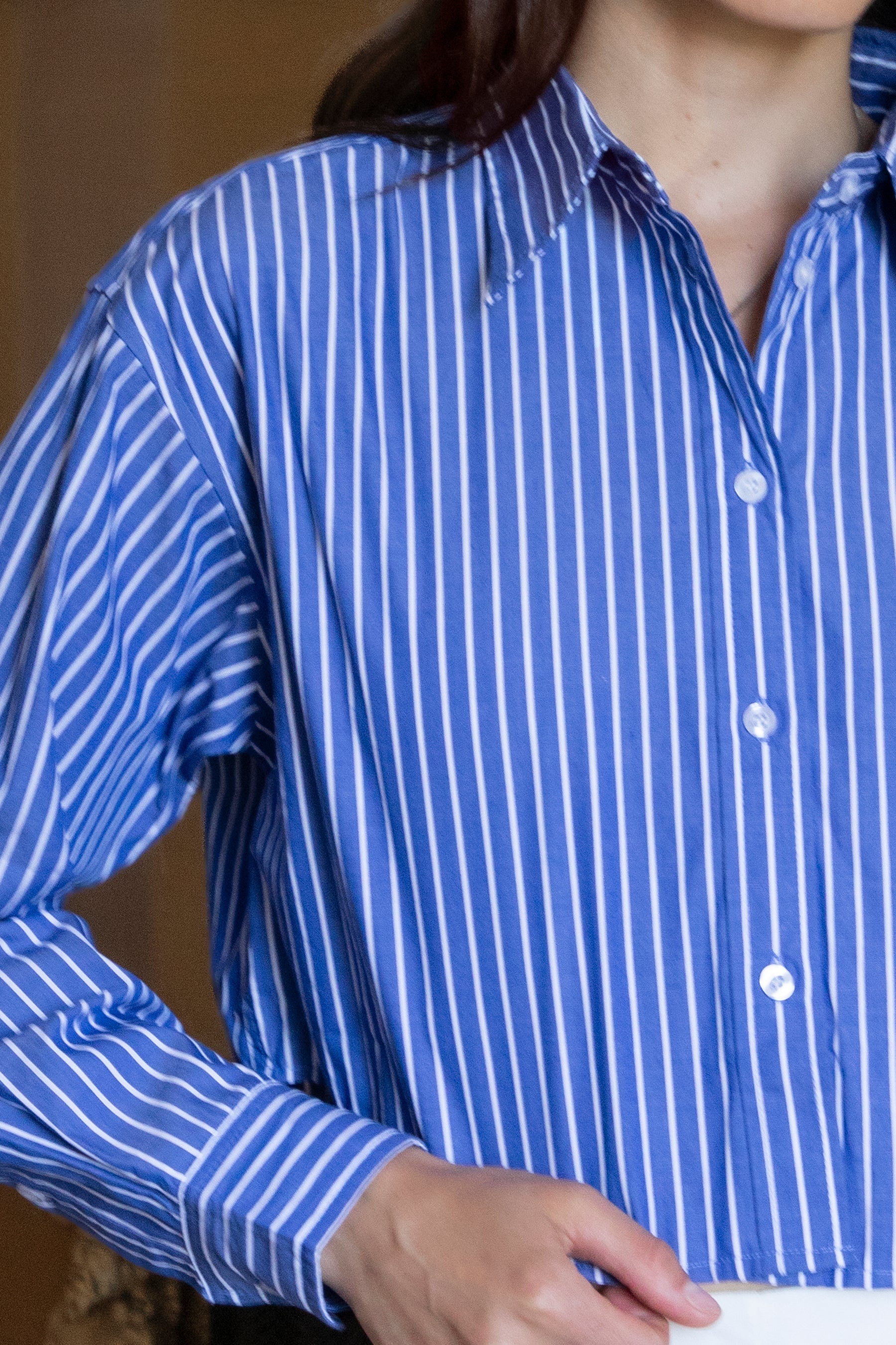 Woman wearing HAMPTON classic stripe collared cropped poplin shirt featuring classic stripe cotton fabric, crisp point collar, button front closure, ultra cropped relaxed silhouette, dropped shoulders, long sleeves with button cuffs, and clean back yoke detail for a polished modern tailored look.