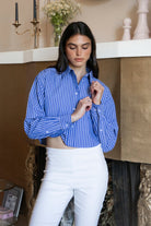 Woman wearing HAMPTON classic stripe collared cropped poplin shirt featuring classic stripe cotton fabric, crisp point collar, button front closure, ultra cropped relaxed silhouette, dropped shoulders, long sleeves with button cuffs, and clean back yoke detail for a polished modern tailored look.