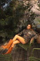 Woman wearing TIC TOC TJ31541-RODEOGIRL RODEOGIRL dark camo cloud fleece hoodie featuring an allover Bayou camo print, oversized relaxed hoodie silhouette, soft cozy cloud fleece fabric, dropped shoulder long sleeves, adjustable drawstring hood, and RODEO GIRL graphic print detail, styled with casual bottoms for a western streetwear-inspired lounge look.