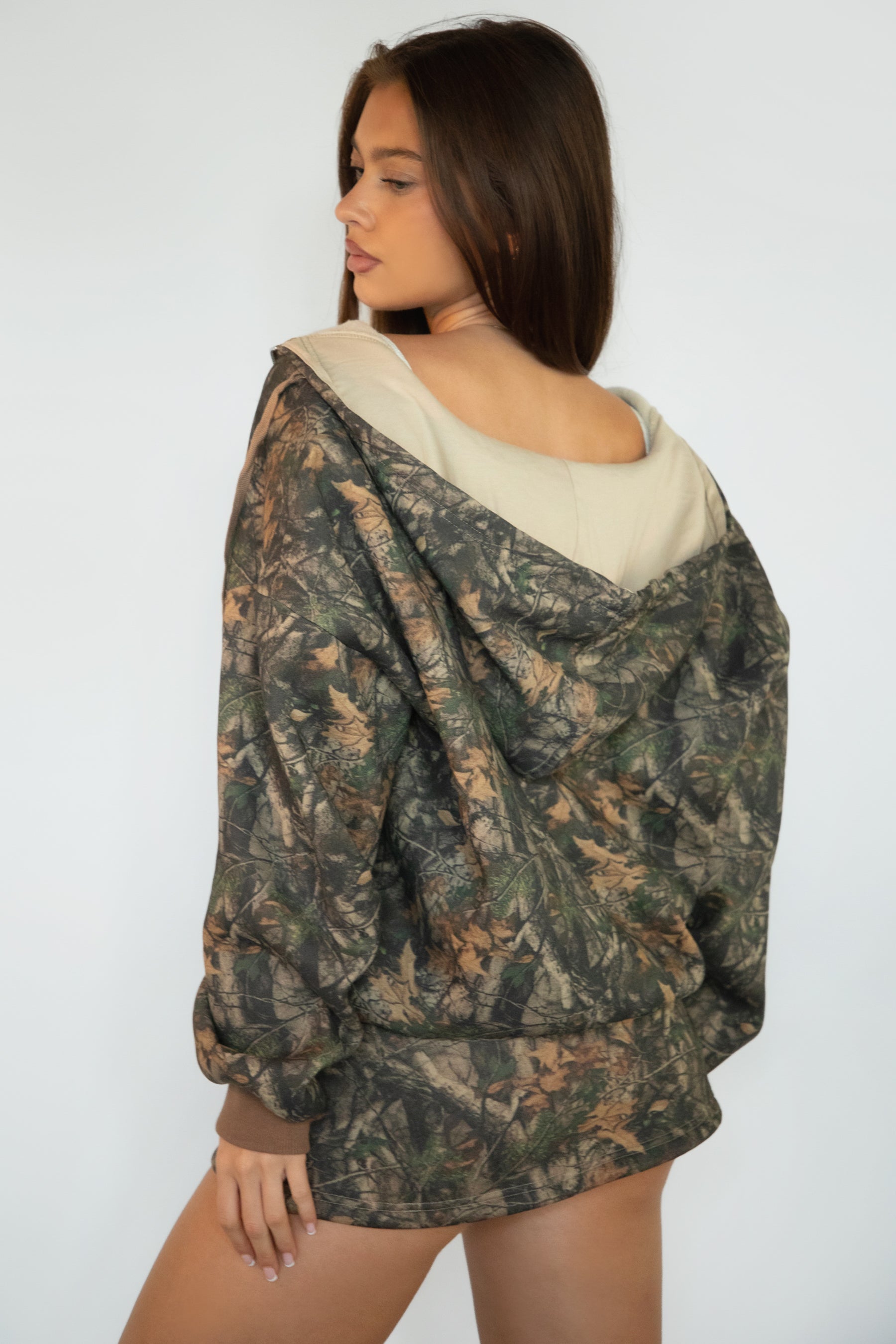 Woman wearing TIC TOC TJ31823-BAYOU-JK BAYOU dark woodland camo fleece zip up hoodie featuring an oversized relaxed fit, full zip front closure, attached drawstring hood, front kangaroo pocket, and ribbed cuffs and hem, styled with casual bottoms for a cozy everyday lounge-and-street look.